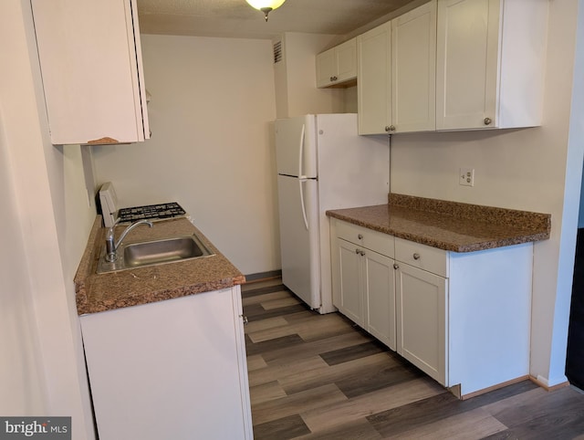 kitchen with dark stone countertops, sink, white cabinetry, dark wood-type flooring, and white refrigerator