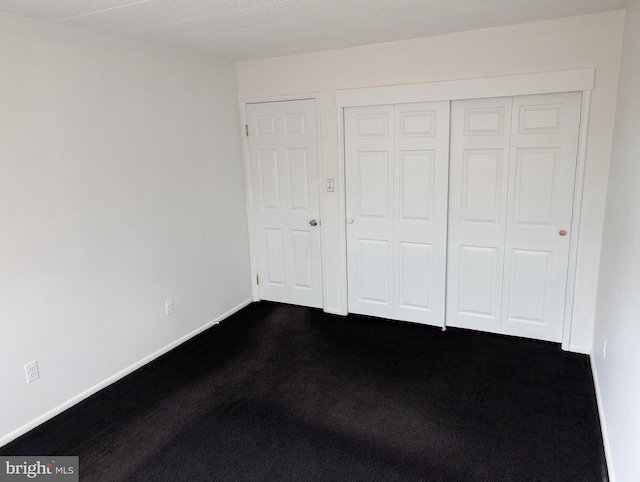 unfurnished bedroom with a closet and dark colored carpet