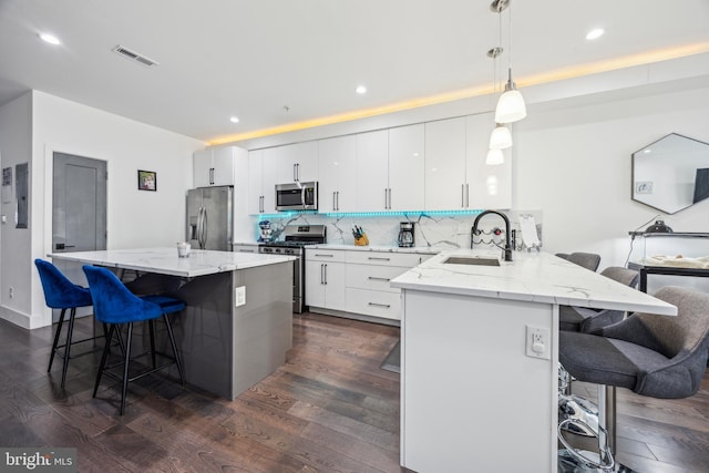 kitchen featuring appliances with stainless steel finishes, a breakfast bar, decorative light fixtures, sink, and white cabinets