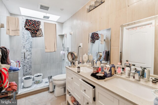 bathroom featuring tile patterned floors, toilet, a shower with shower door, tile walls, and vanity