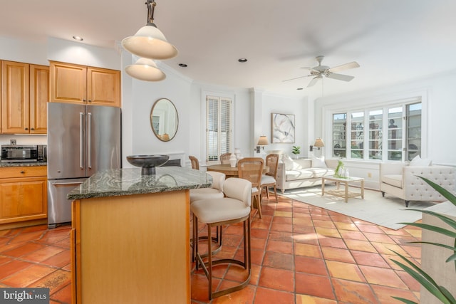 kitchen featuring pendant lighting, a breakfast bar, ceiling fan, appliances with stainless steel finishes, and dark stone countertops