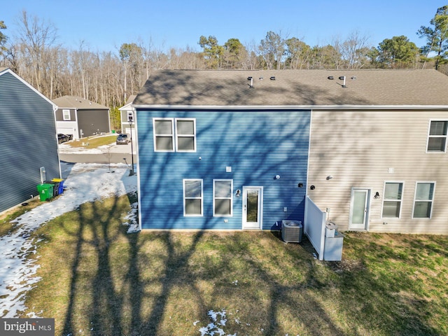 rear view of property with central AC unit and a lawn