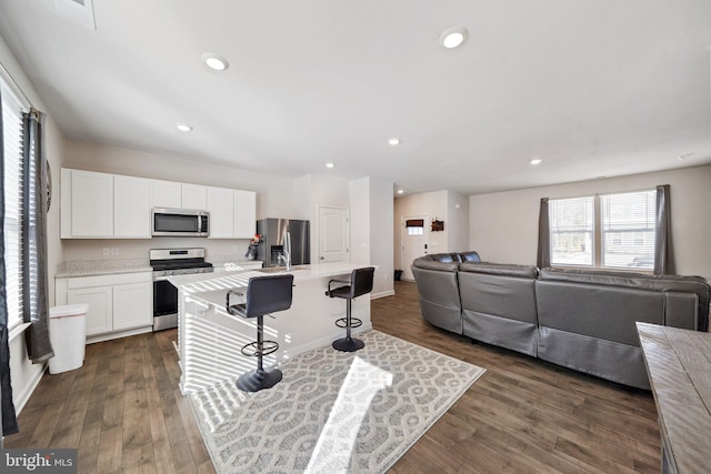 kitchen featuring dark hardwood / wood-style floors, a center island with sink, a breakfast bar, white cabinetry, and stainless steel appliances