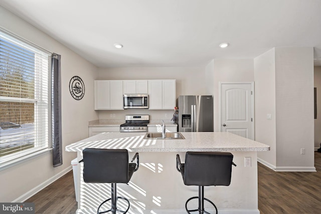 kitchen with a kitchen bar, sink, a kitchen island with sink, stainless steel appliances, and white cabinets