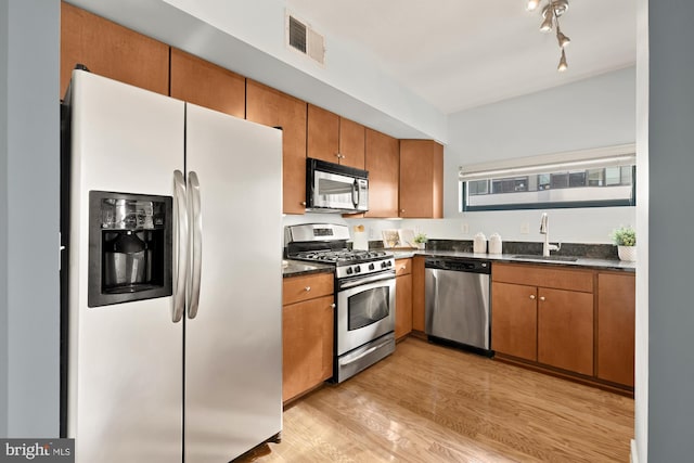 kitchen featuring appliances with stainless steel finishes, sink, dark stone countertops, and light hardwood / wood-style floors