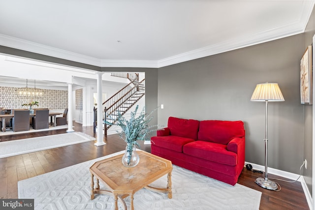 living room featuring decorative columns, wood-type flooring, ornamental molding, and an inviting chandelier