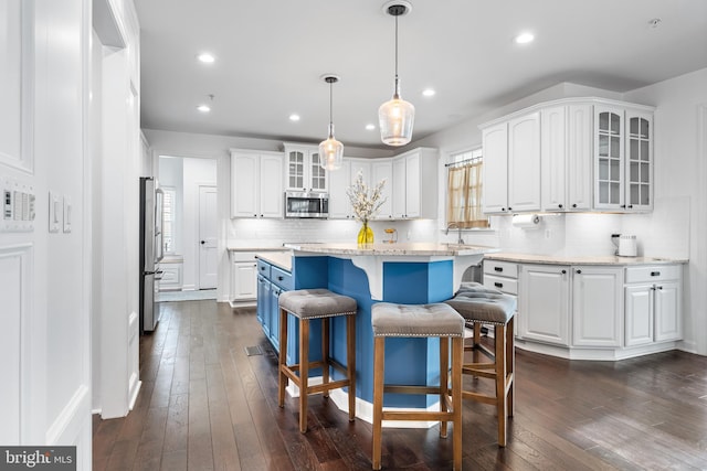 kitchen featuring pendant lighting, appliances with stainless steel finishes, a center island, white cabinetry, and backsplash