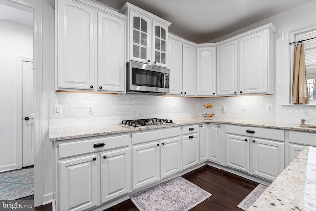 kitchen featuring dark hardwood / wood-style flooring, backsplash, white cabinetry, light stone counters, and stainless steel appliances