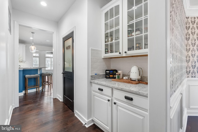 bar with white cabinets, dark hardwood / wood-style floors, light stone counters, and pendant lighting