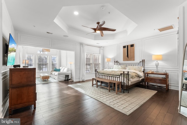 bedroom featuring ceiling fan, multiple windows, a tray ceiling, and dark hardwood / wood-style floors