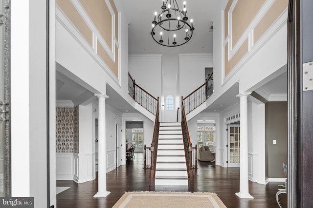 foyer entrance featuring ornamental molding, a towering ceiling, ornate columns, and dark wood-type flooring