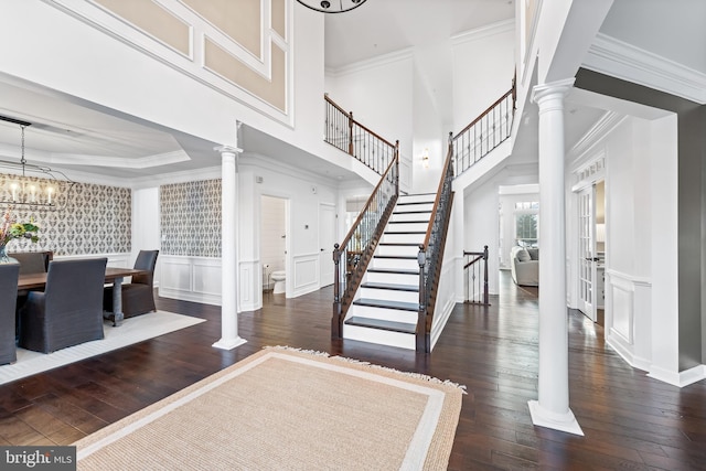 foyer entrance featuring crown molding, decorative columns, a chandelier, and dark hardwood / wood-style flooring