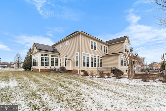 snow covered rear of property with a sunroom, central AC, and solar panels