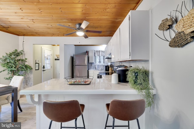 kitchen featuring white cabinets, wood ceiling, tasteful backsplash, a kitchen breakfast bar, and stainless steel refrigerator