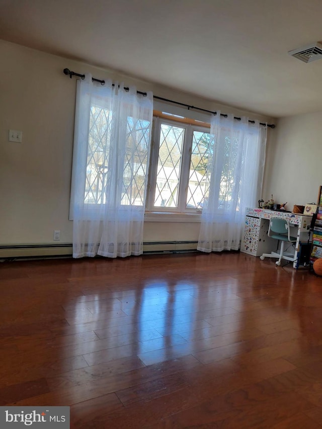 spare room featuring baseboard heating and dark hardwood / wood-style floors