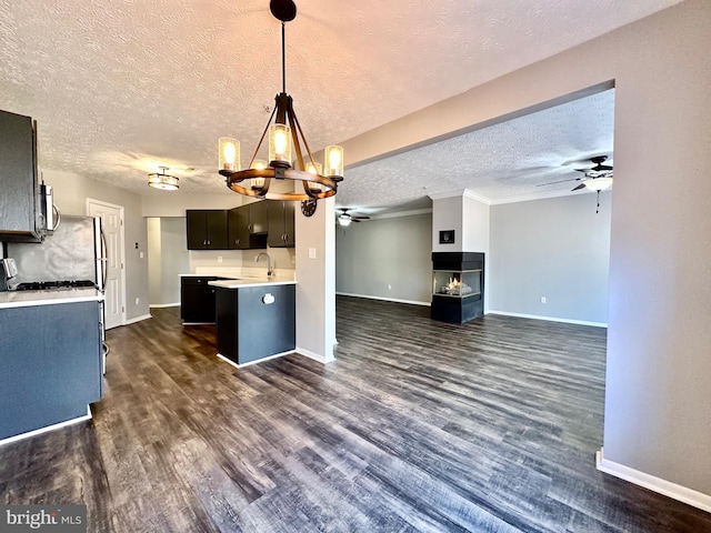 kitchen featuring hanging light fixtures, a textured ceiling, a multi sided fireplace, dark hardwood / wood-style flooring, and ceiling fan with notable chandelier