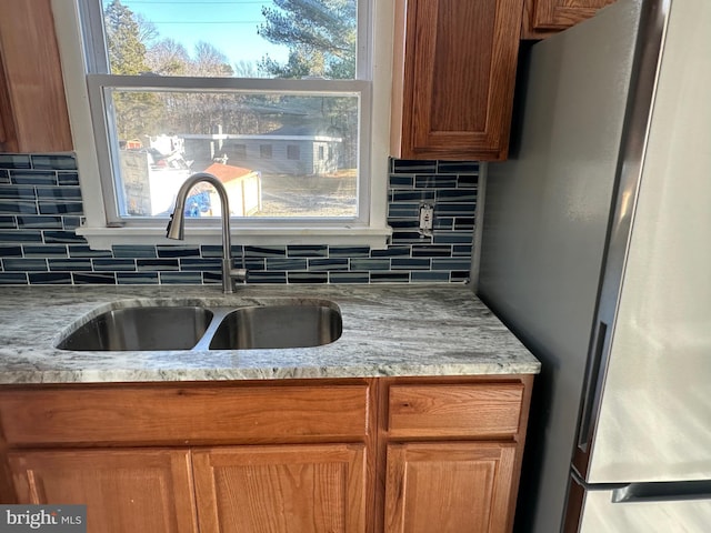 kitchen featuring backsplash, stainless steel fridge, light stone counters, and sink