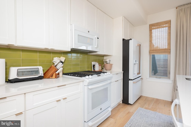 kitchen with tasteful backsplash, white cabinets, light wood-type flooring, and white appliances