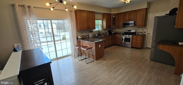 kitchen with sink, light wood-type flooring, a breakfast bar, a chandelier, and stainless steel appliances