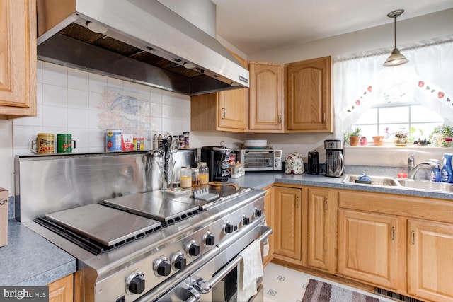 kitchen featuring wall chimney range hood, hanging light fixtures, sink, and stainless steel stove