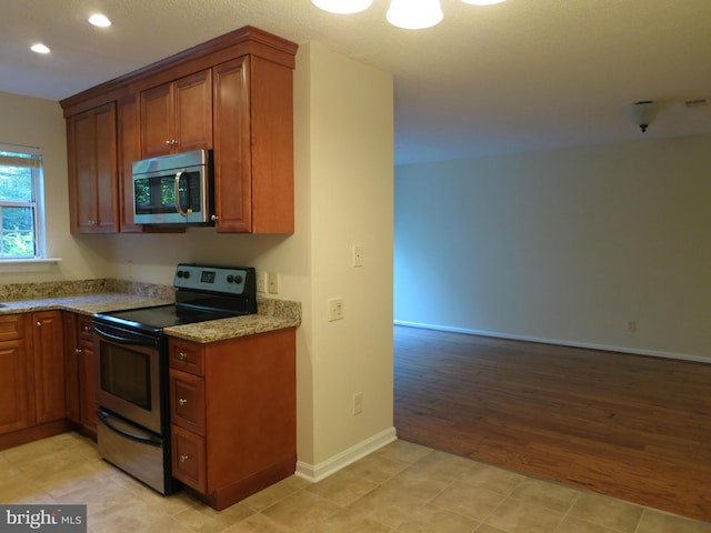 kitchen with light wood finished floors, light stone countertops, brown cabinets, and appliances with stainless steel finishes