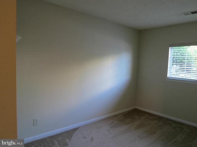 spare room with a textured ceiling, carpet floors, visible vents, and baseboards