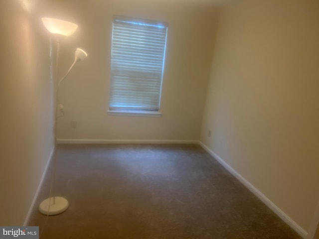 empty room with baseboards and dark colored carpet