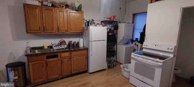 kitchen with sink, white appliances, stacked washer and clothes dryer, and light wood-type flooring