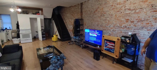 living room with a notable chandelier, brick wall, and light hardwood / wood-style flooring