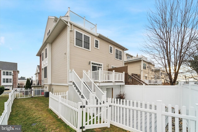 back of property with a deck, central air condition unit, and a yard