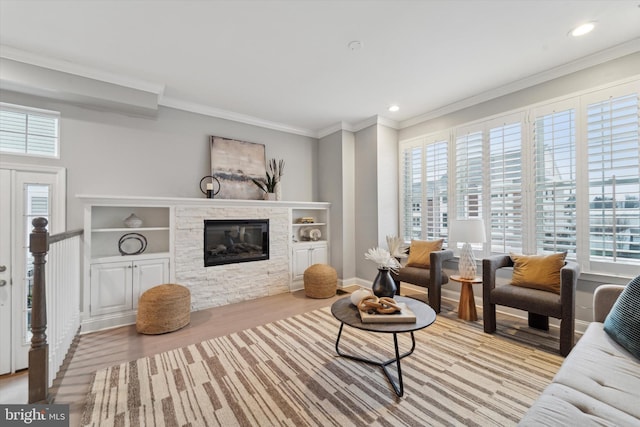 living room featuring light hardwood / wood-style floors, a wealth of natural light, ornamental molding, and a stone fireplace