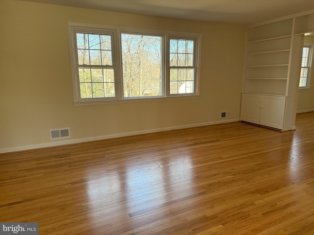 empty room featuring visible vents, plenty of natural light, baseboards, and wood finished floors