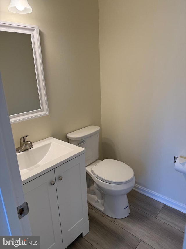 half bathroom with baseboards, vanity, toilet, and wood finished floors