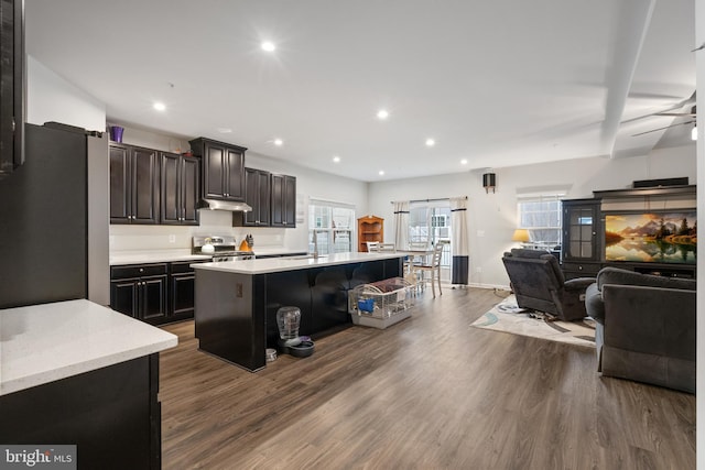 kitchen with dark hardwood / wood-style floors, a kitchen bar, stainless steel appliances, dark brown cabinets, and a center island with sink