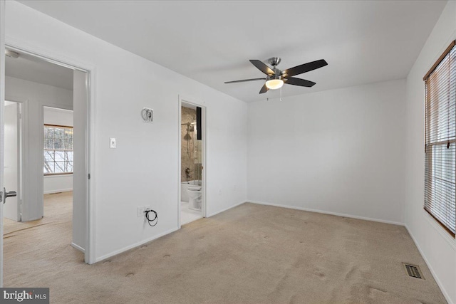 unfurnished bedroom featuring ceiling fan, ensuite bath, and light colored carpet