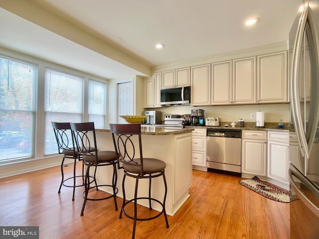 kitchen with a center island, stainless steel appliances, dark stone counters, and light hardwood / wood-style flooring