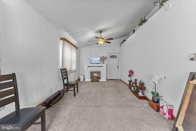 carpeted living area featuring a textured ceiling, a ceiling fan, baseboards, vaulted ceiling, and a glass covered fireplace