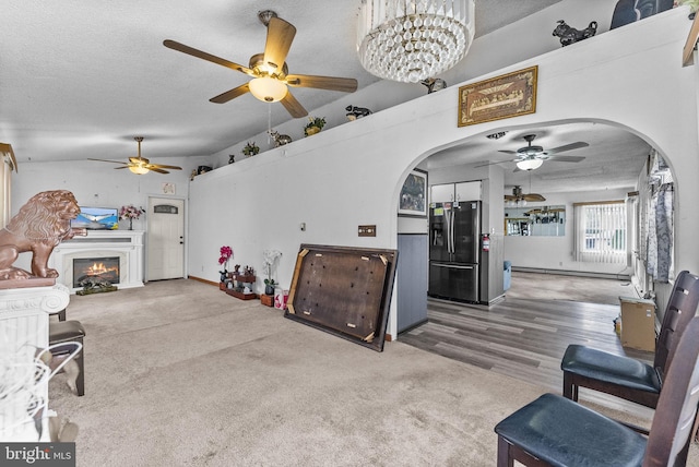 living room featuring arched walkways, a textured ceiling, lofted ceiling, a baseboard heating unit, and a glass covered fireplace