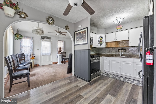 kitchen featuring arched walkways, wood finished floors, a sink, white cabinetry, and appliances with stainless steel finishes