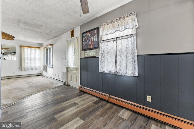 unfurnished room featuring a textured ceiling, baseboard heating, wood finished floors, and a ceiling fan