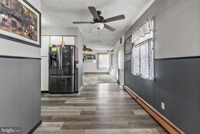 hall featuring wainscoting, a baseboard heating unit, a textured ceiling, and wood finished floors