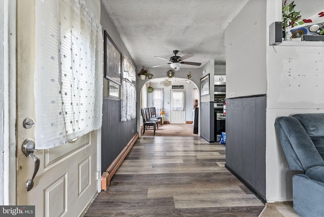 foyer entrance with arched walkways, a ceiling fan, wood finished floors, a textured ceiling, and a baseboard heating unit