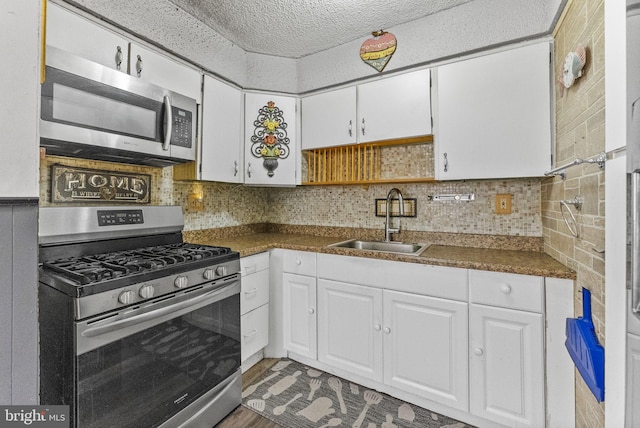 kitchen featuring white cabinets, dark countertops, a sink, stainless steel appliances, and backsplash