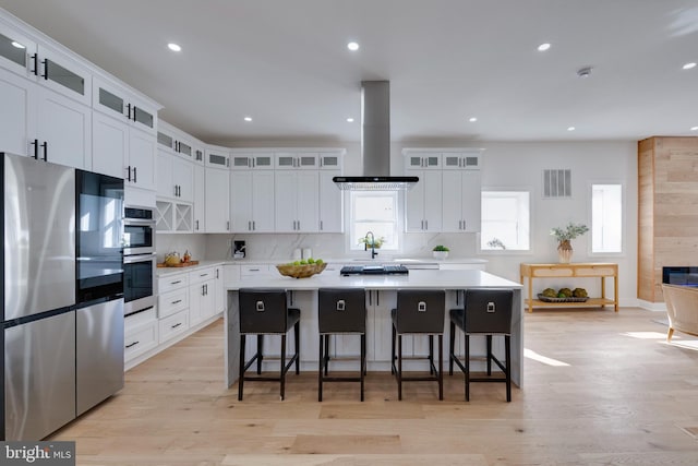 kitchen with appliances with stainless steel finishes, white cabinets, a kitchen bar, a kitchen island, and island range hood