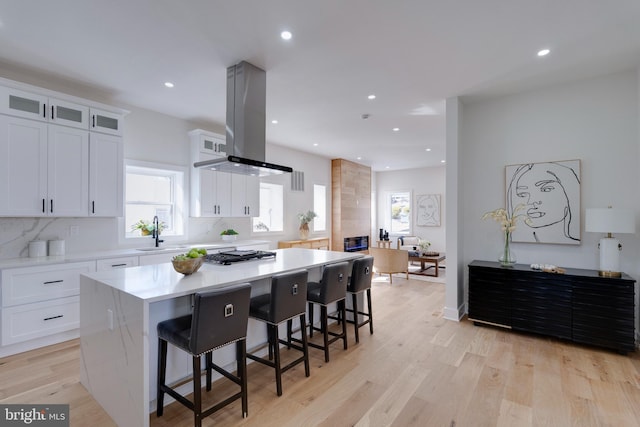 kitchen with a center island, white cabinetry, island exhaust hood, a kitchen breakfast bar, and sink