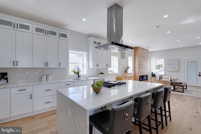 kitchen with white cabinetry, island range hood, sink, a kitchen island, and a breakfast bar area