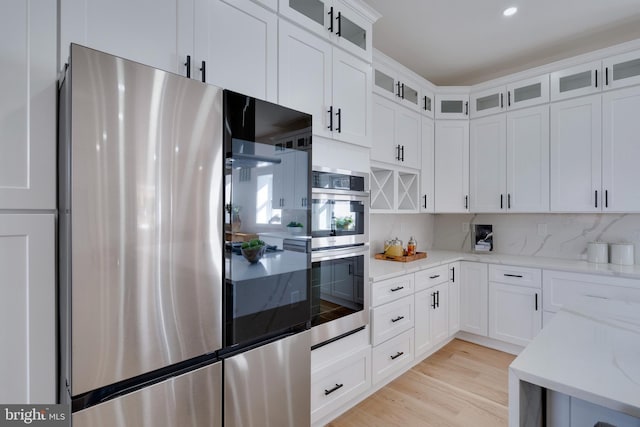 kitchen with light stone countertops, white cabinets, appliances with stainless steel finishes, and tasteful backsplash