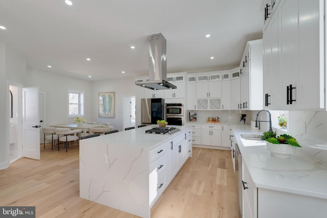 kitchen with white cabinets, appliances with stainless steel finishes, a center island, and island exhaust hood