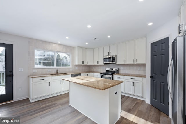 kitchen with light stone countertops, appliances with stainless steel finishes, a kitchen island, wood-type flooring, and white cabinetry