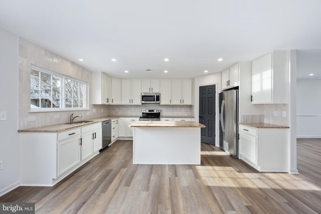 kitchen featuring light hardwood / wood-style flooring, appliances with stainless steel finishes, white cabinets, a kitchen island, and light stone counters